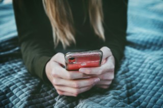 Eine Person mit langen Harren hält ein Handy in der Hand